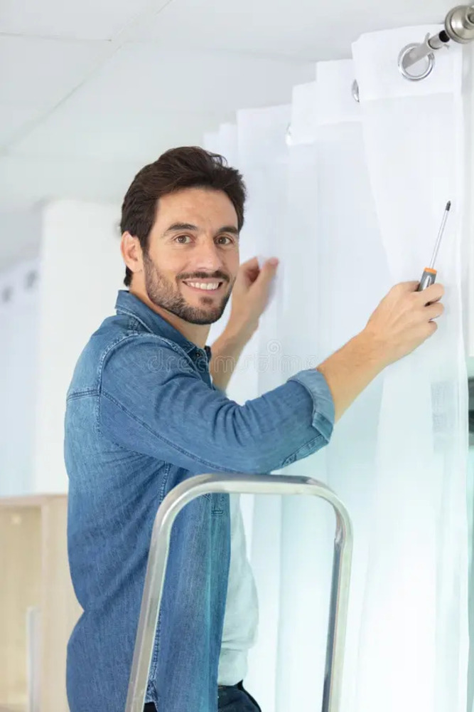 2young man installing curtains over window young young man installing curtains over window 258026054